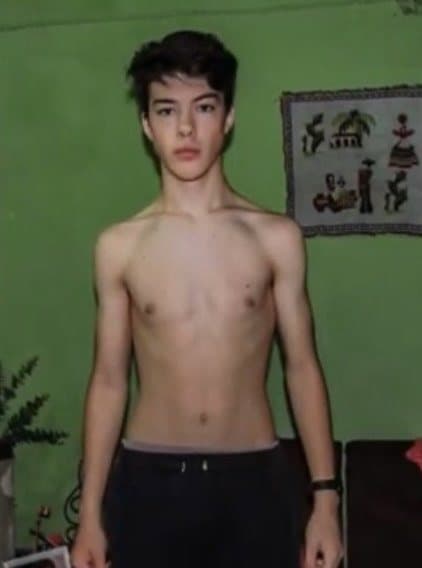 Facundo de adolescente, muy flaco, sin remera frente a una pared verde